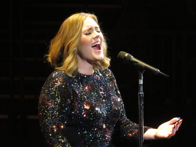 Adele is shown performing at a concert.