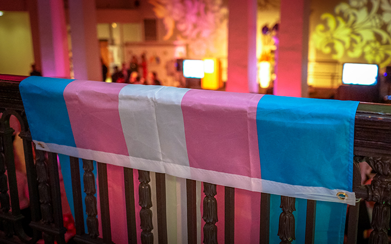 A transgender flag with pink, blue, and white colors is shown hanging from a banister.